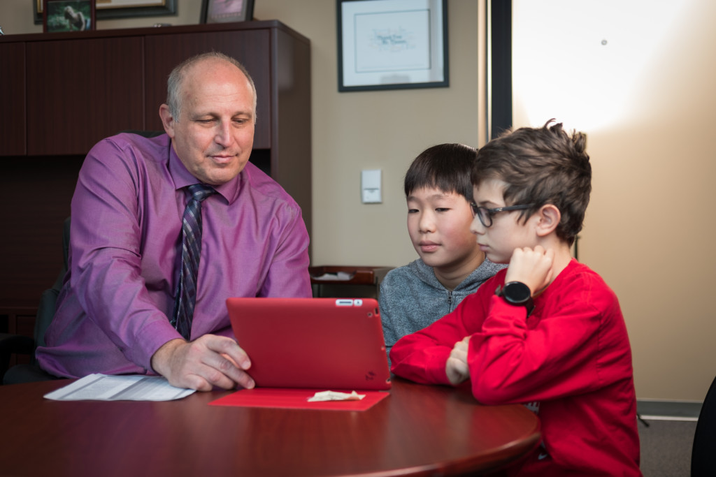 Helmut Tinnes works on a red tablet with two students in an office setting