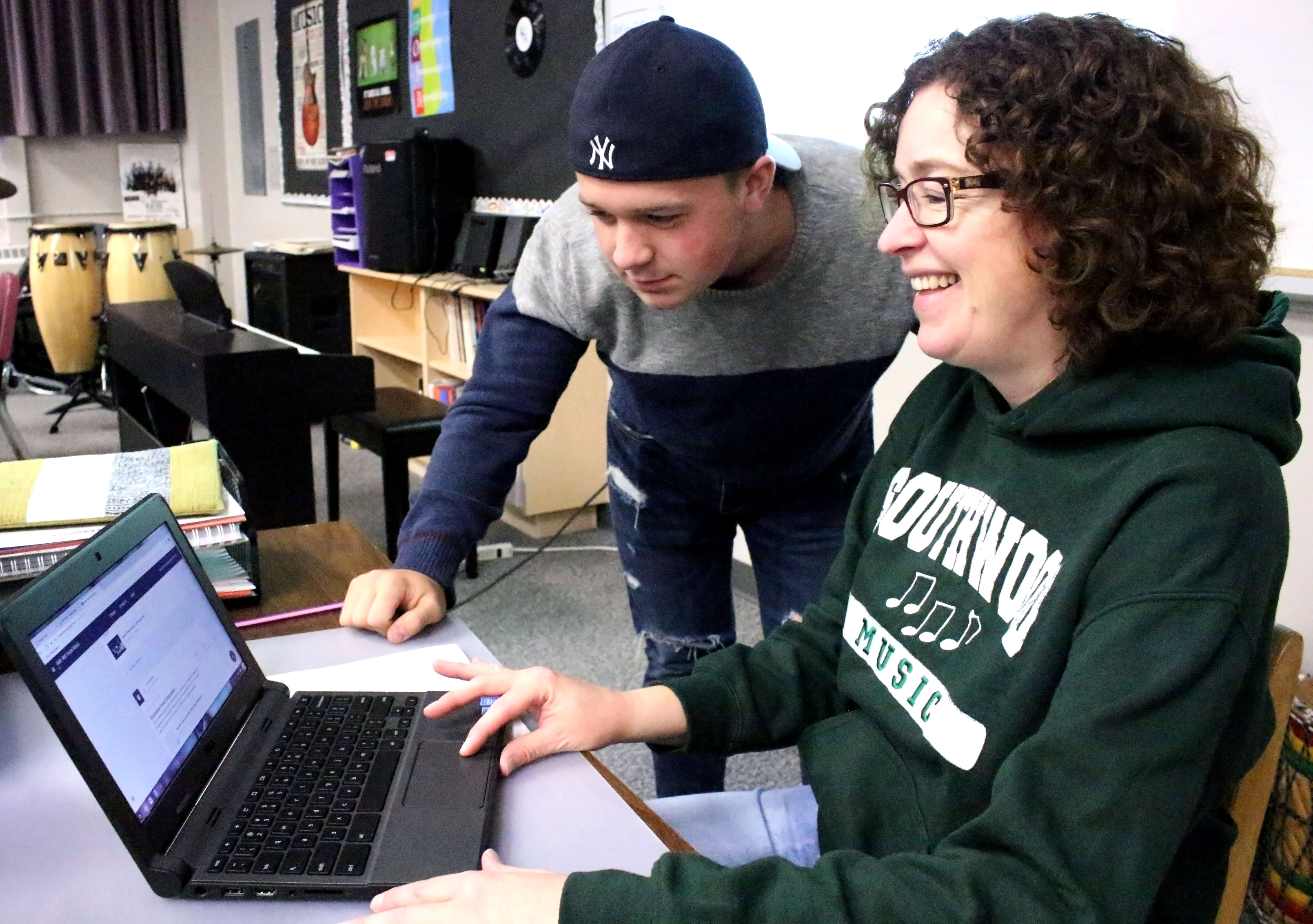 Jane Gingerich works with a student in the classroom on a Chromebook.
