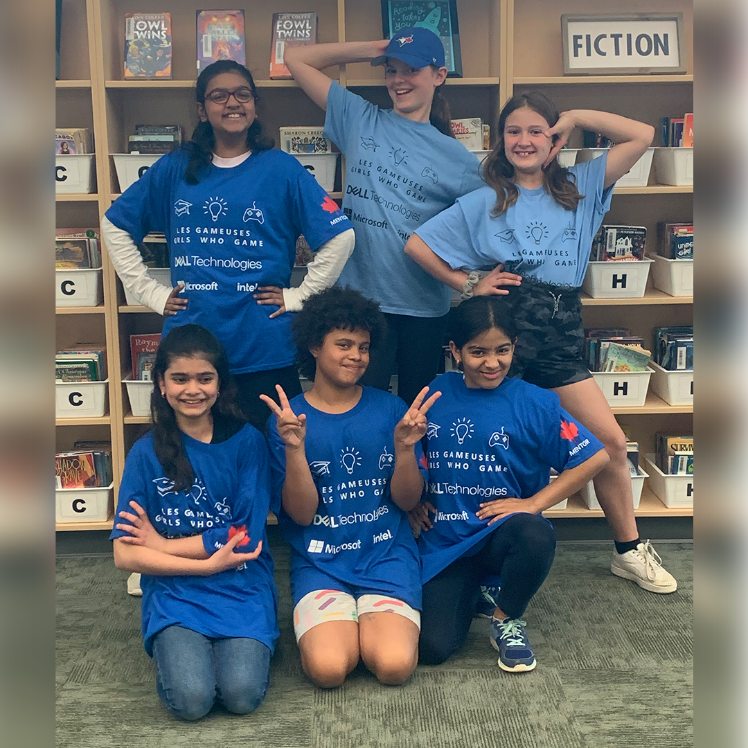 Six students wearing blue strike funny poses in front of a bookshelf. 