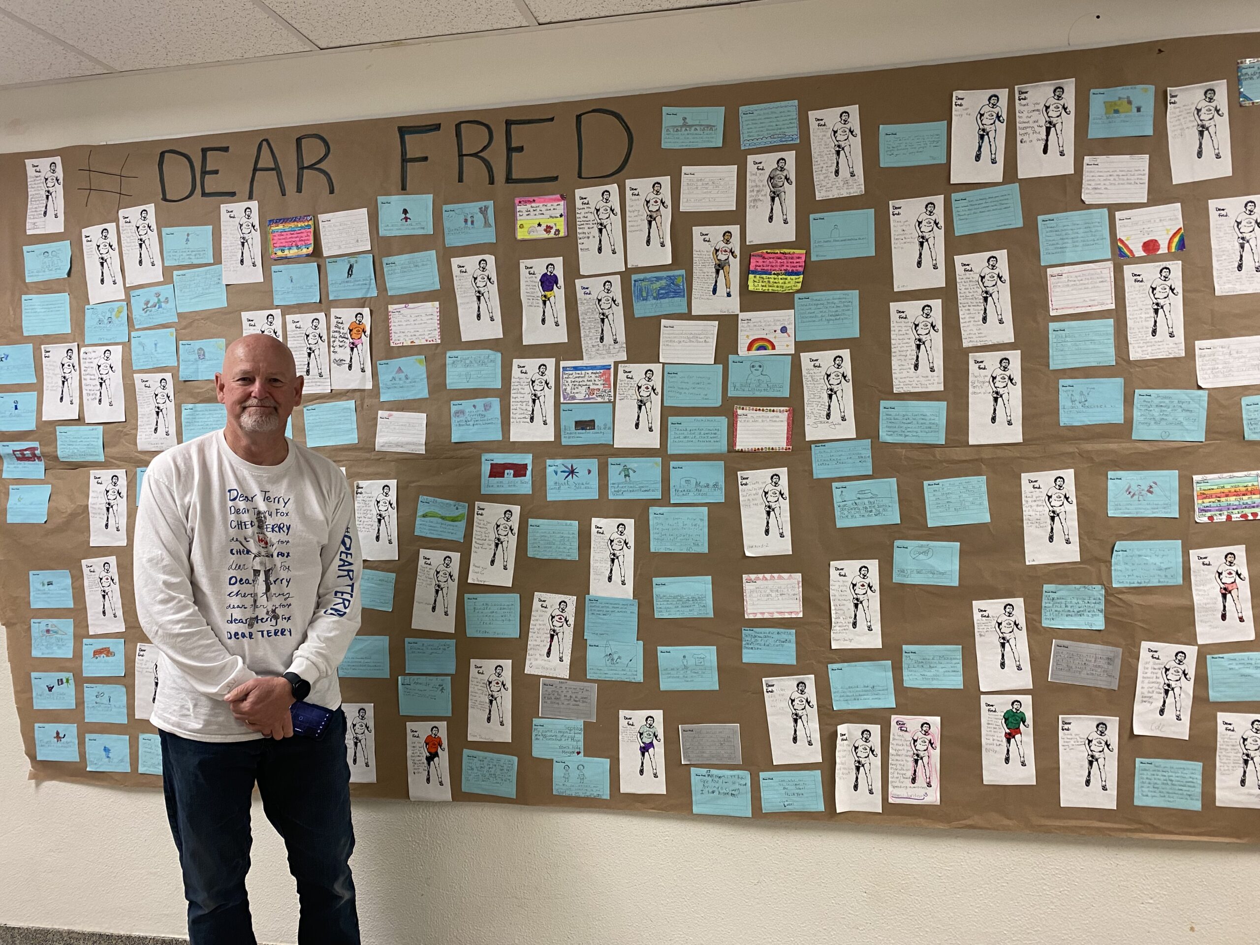 Fred Fox stands in front of a large sign featuring many messages written to him from students. 
