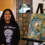 Student Trustee Vaishnave Raina in front of artwork from local artist.