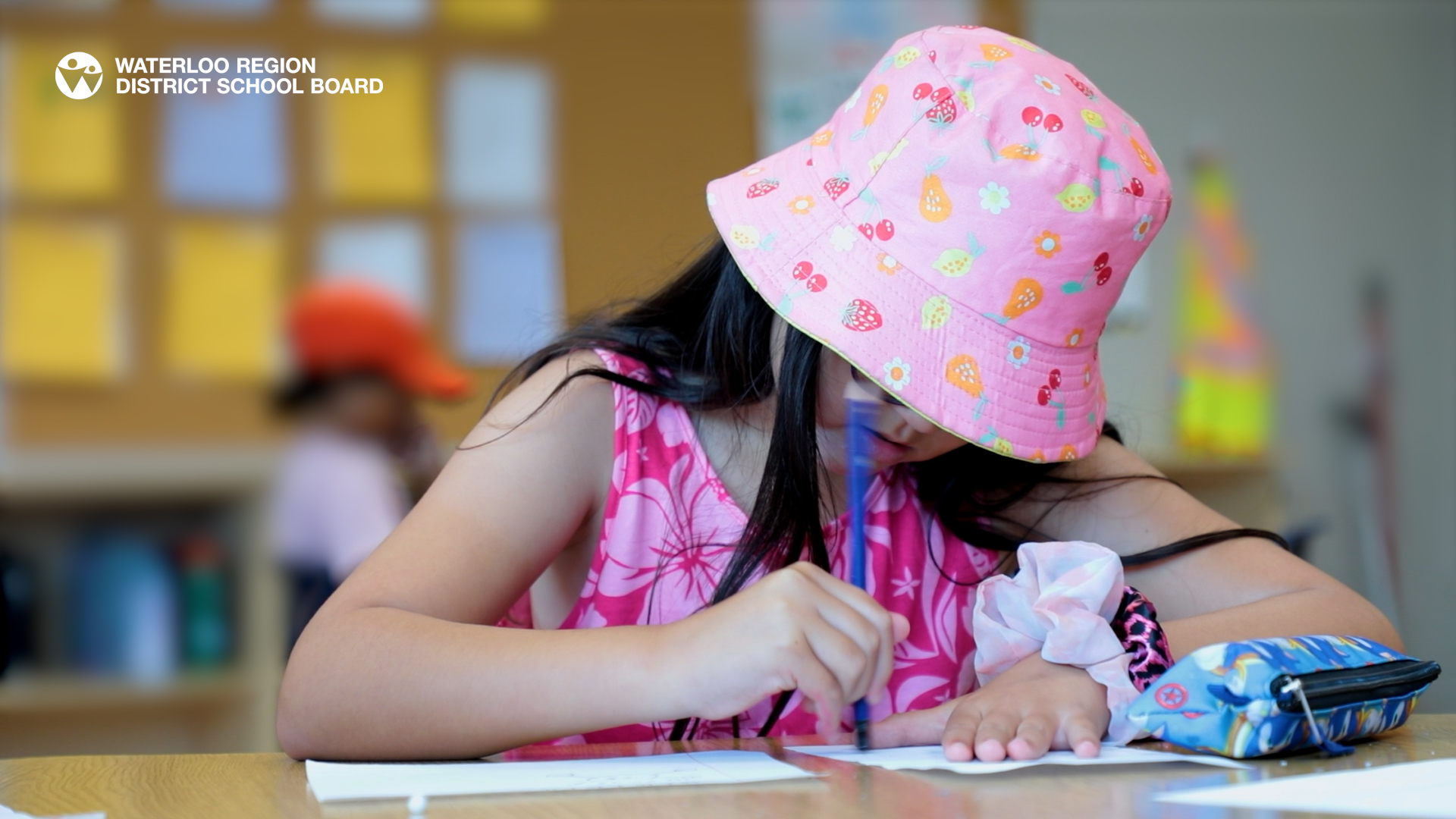 Student wearing a pink bucket hat writing on a piece of paper