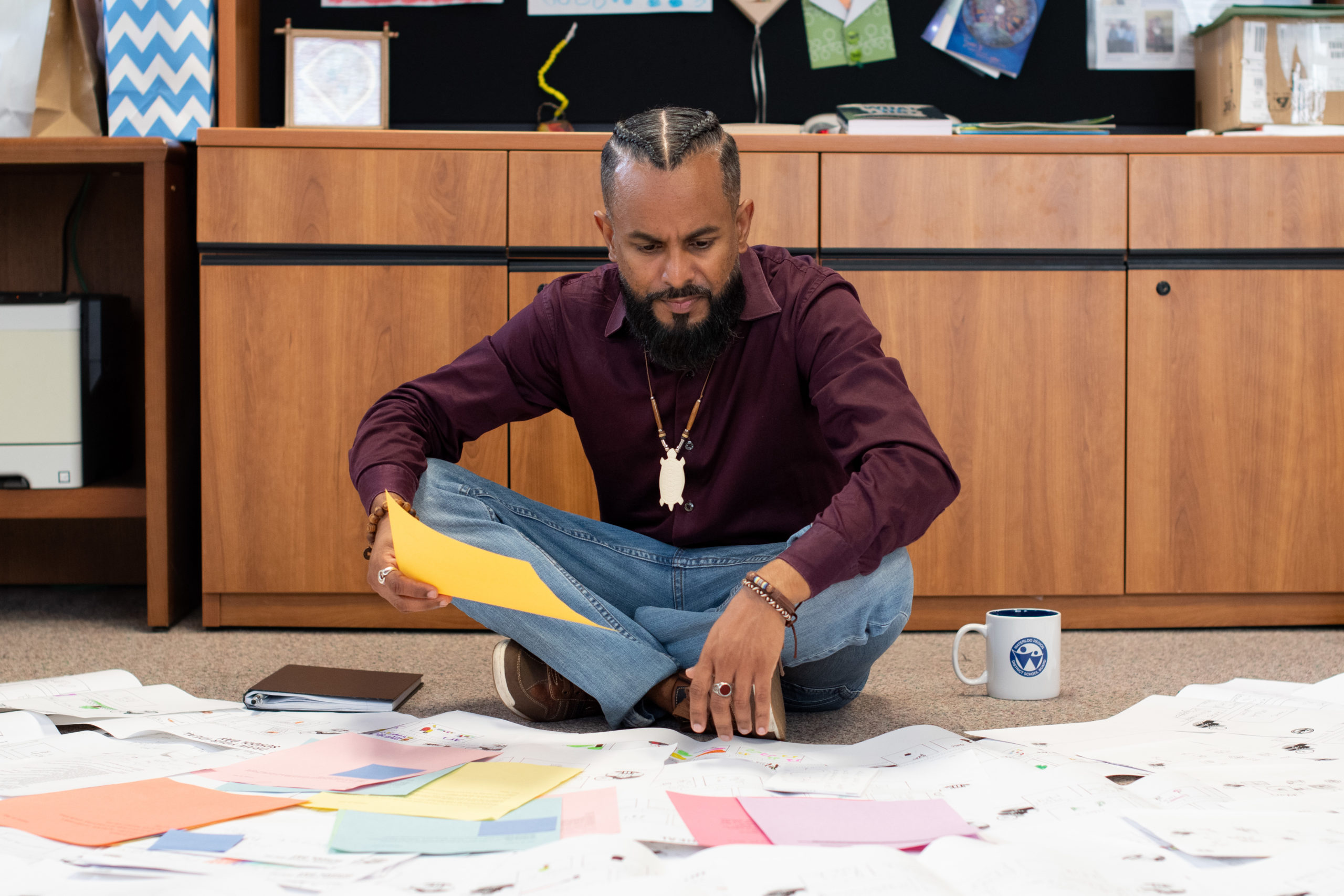 jeewan chanicka, director of education, sits on the floor of his office, surrounded by paper copies of student feedback. He is reading one in his hand.