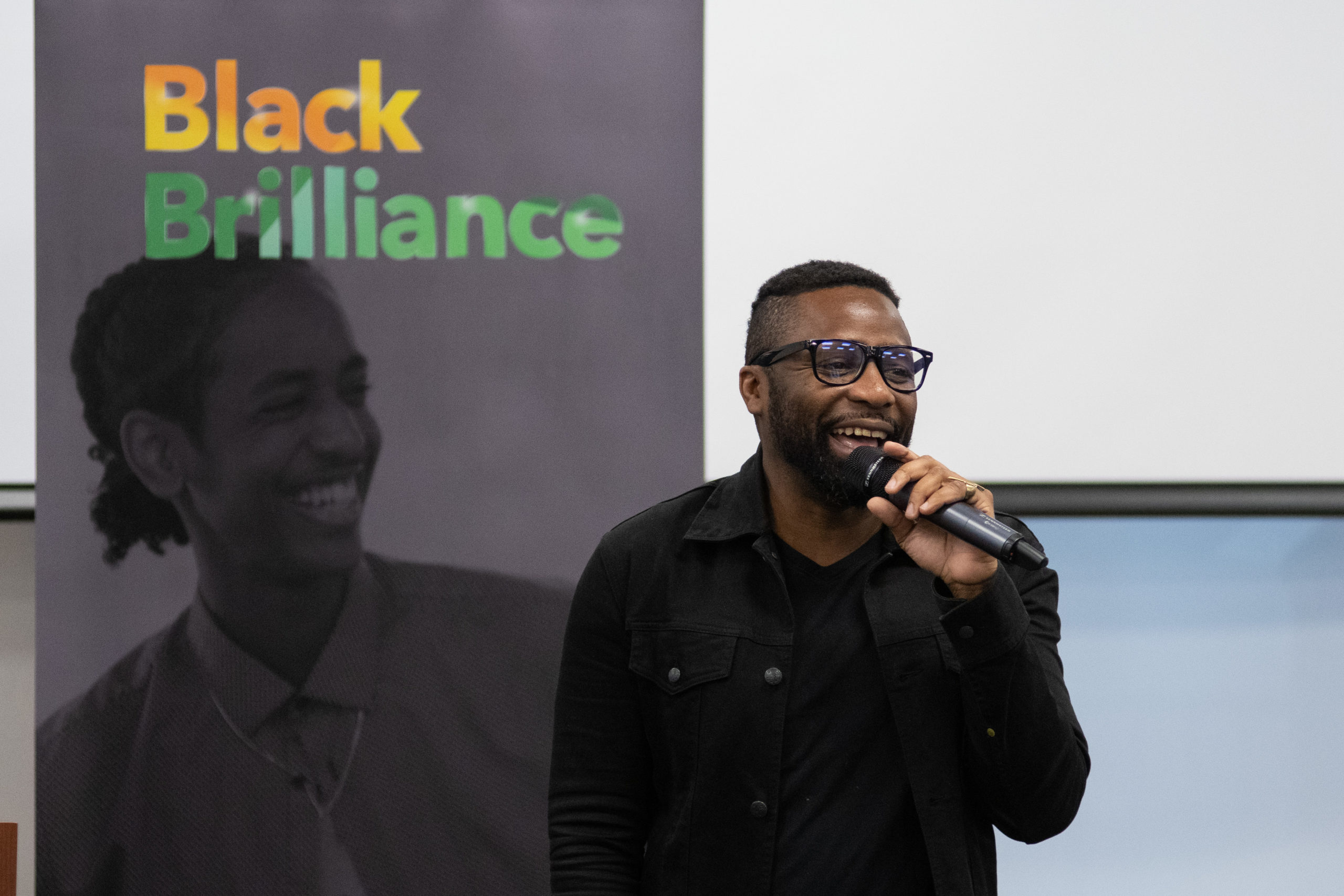 Antonio Michael Downing speaks to students at the Black Brilliance Conference in front of a banner that reads "Black Brilliance". 