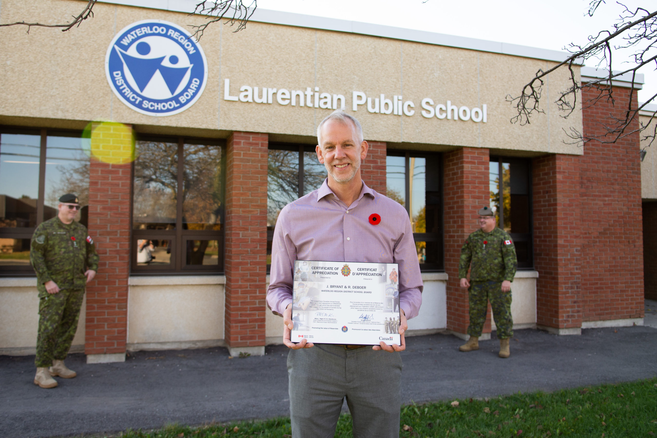 Ron Deboer stands in front of Laurentian Public School with the certificate from the Canadian Forces Liaison Council
