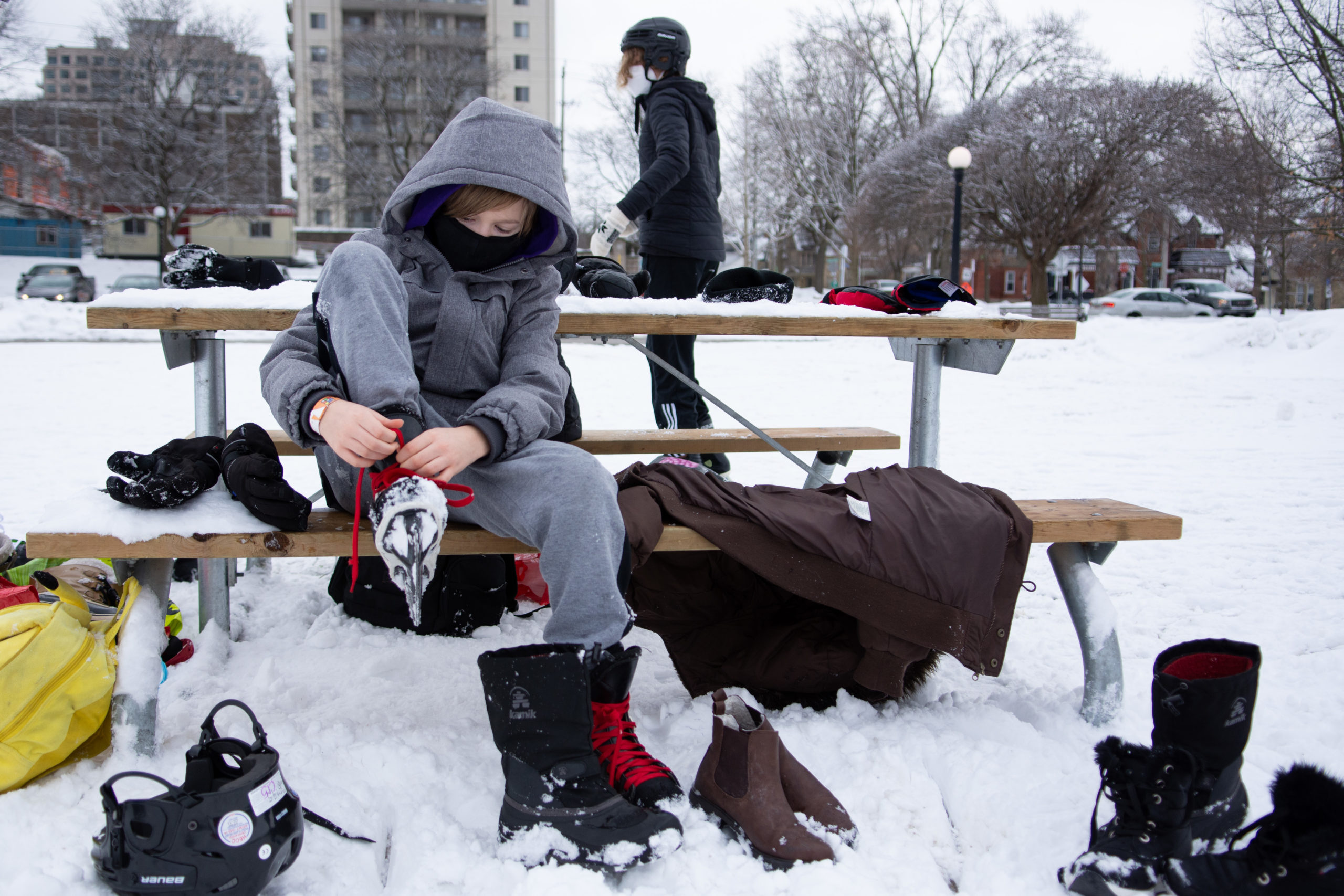 A student removes their skates while sitting on a park bench