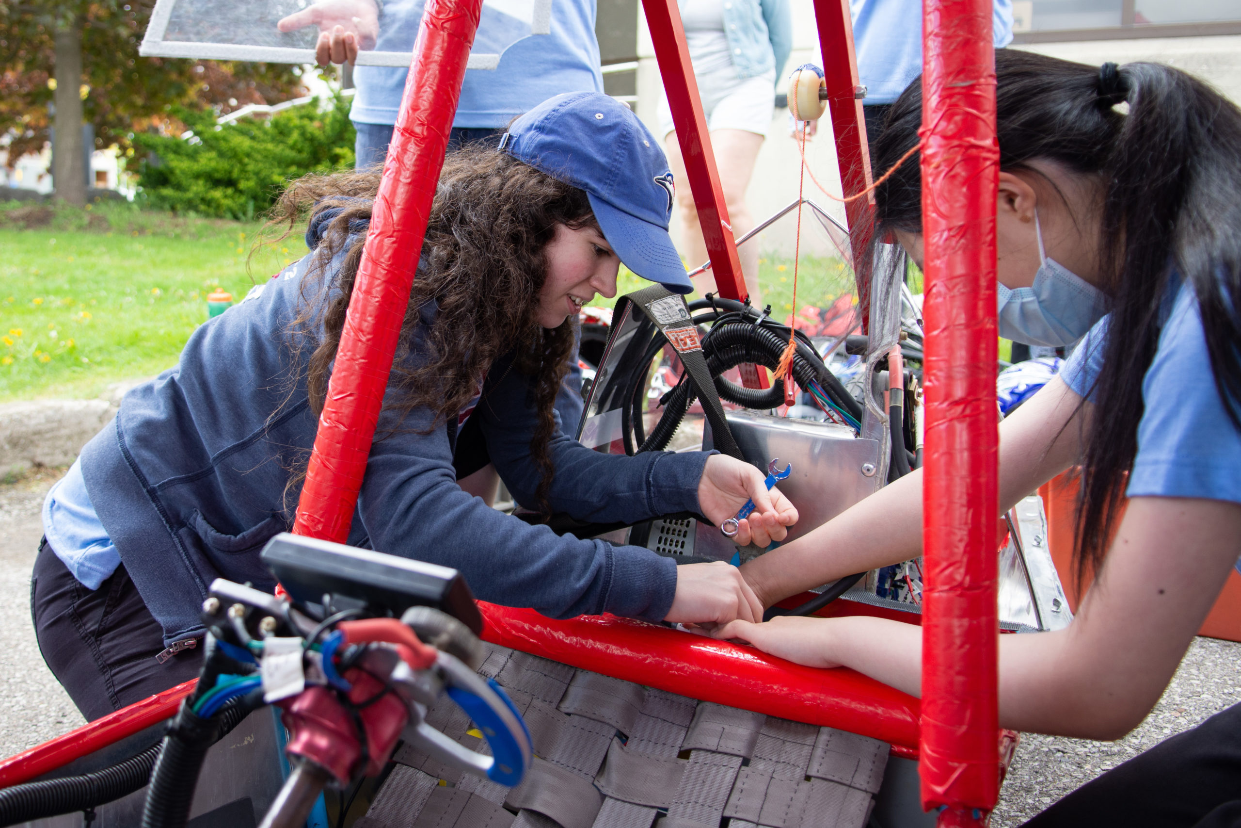 A student leans in between the roll cage on the electric car to work on the battery connection.