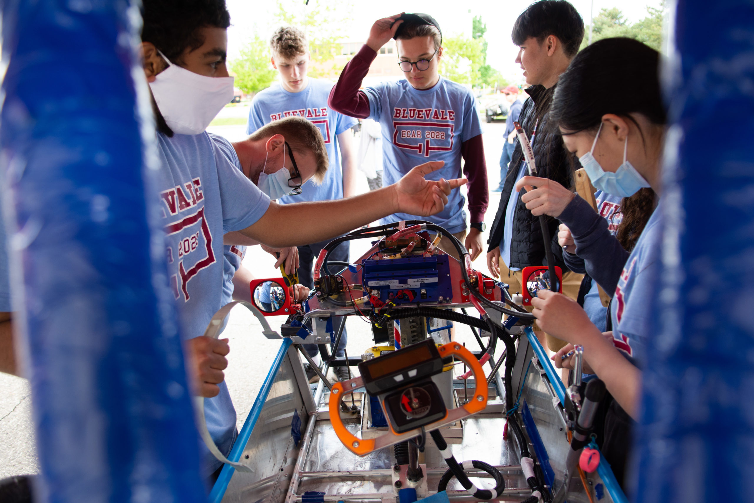 A group of students encircle an electric car, as each of them works on one piece to get it ready for the race.