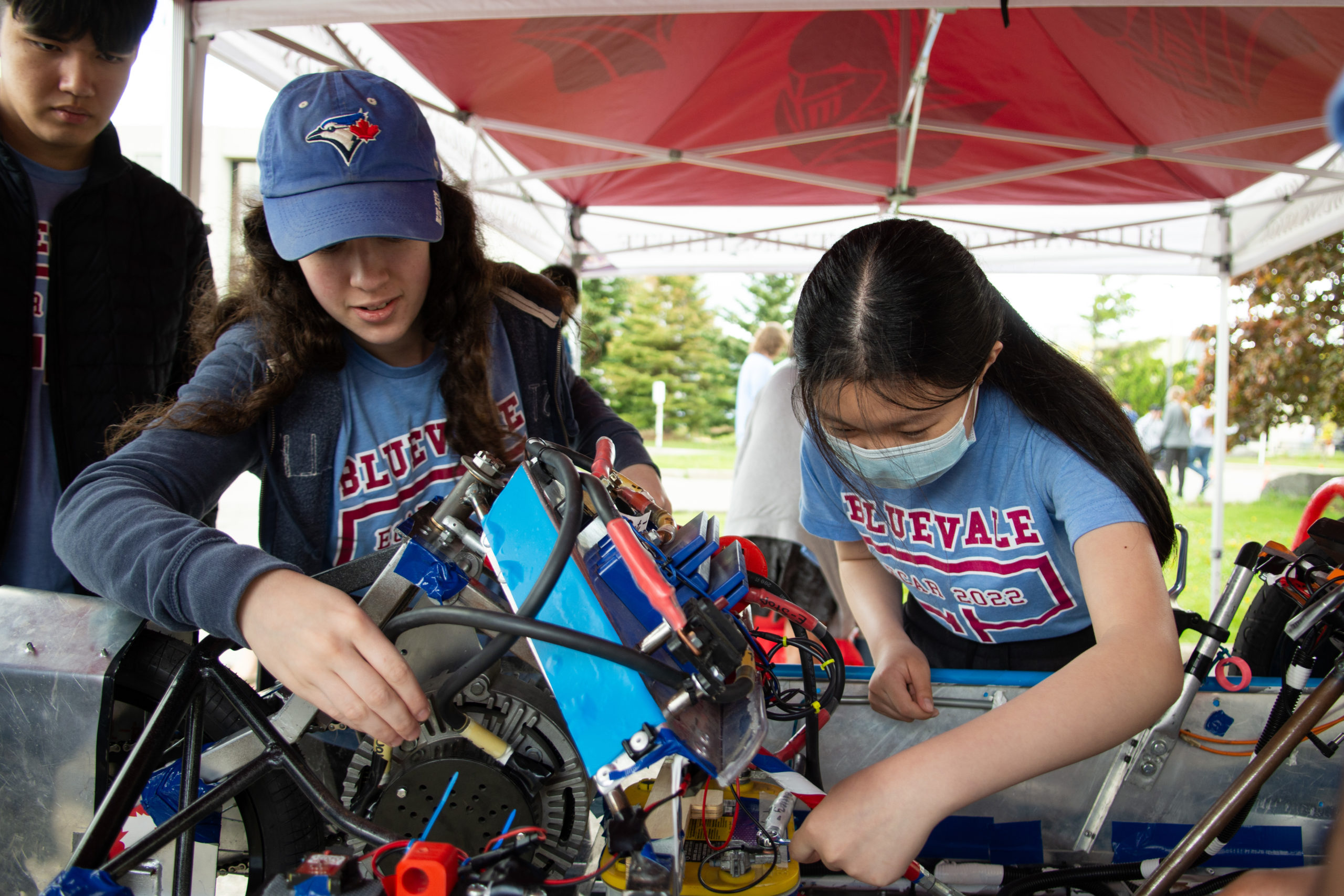 Two students with tools in hand working on an electric car. 