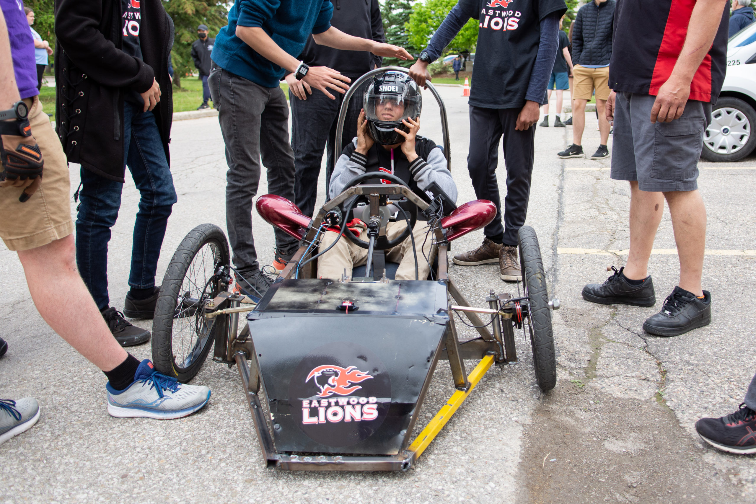 A student in the Eastwood Collegiate Institute car straps his helmet on, surrounded by members of the team. 
