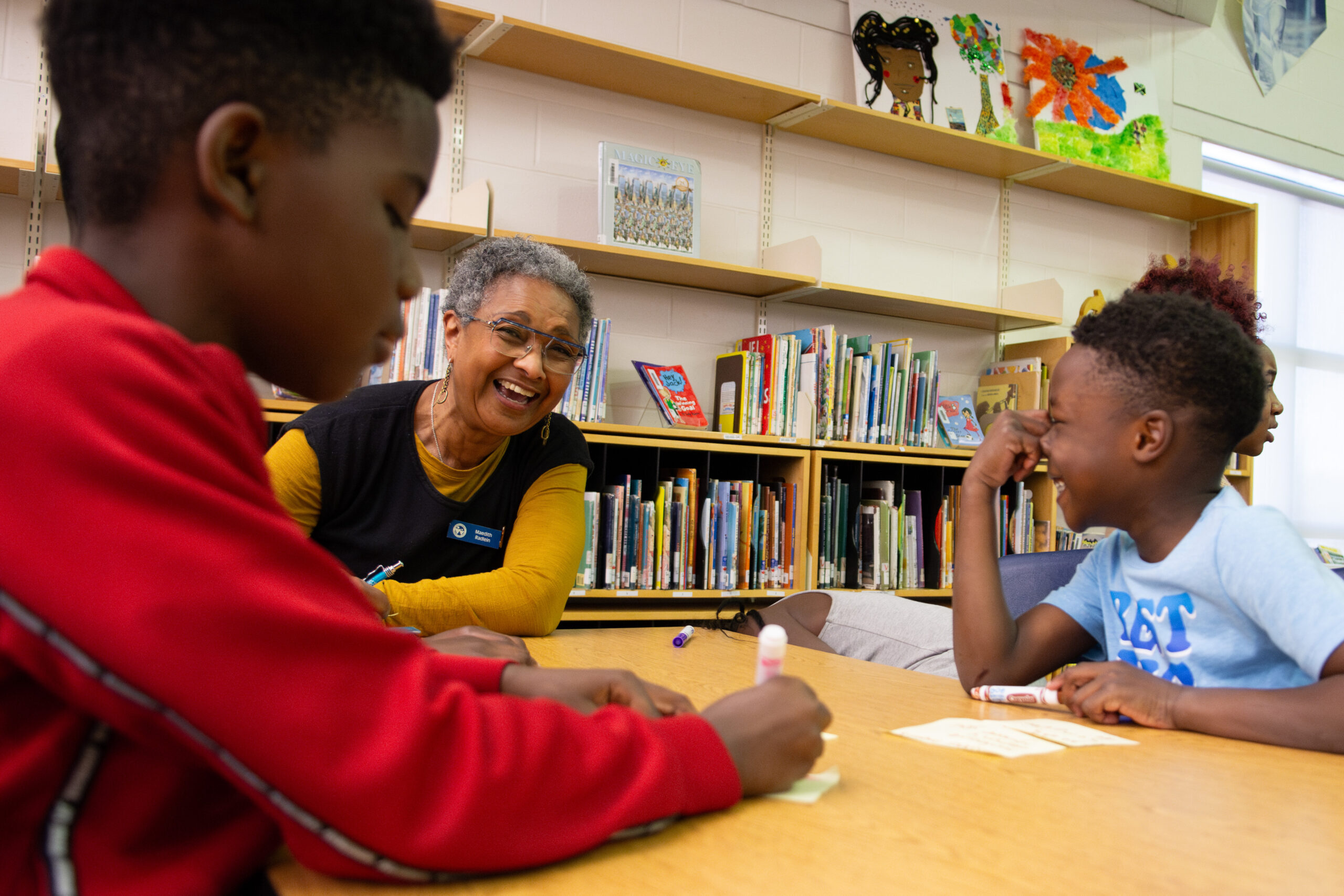 Trustee Raedlin enjoys a laugh with two students at a table in a library. 