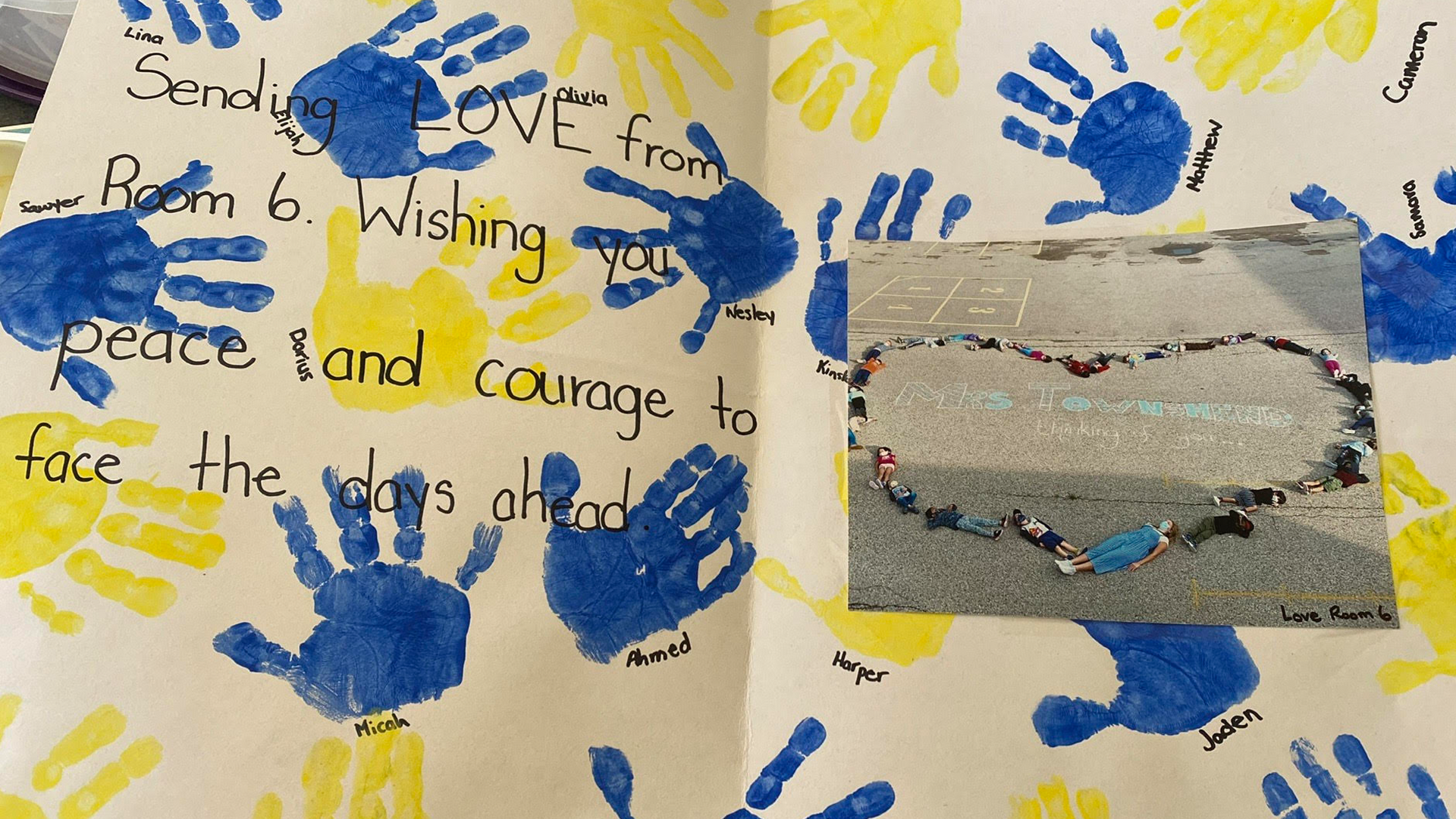 A card shows an image of students laying on tarmac in the shape of a heart along with the message "Sending Love from Room 6. Wishing you peace and courage to face the days ahead."