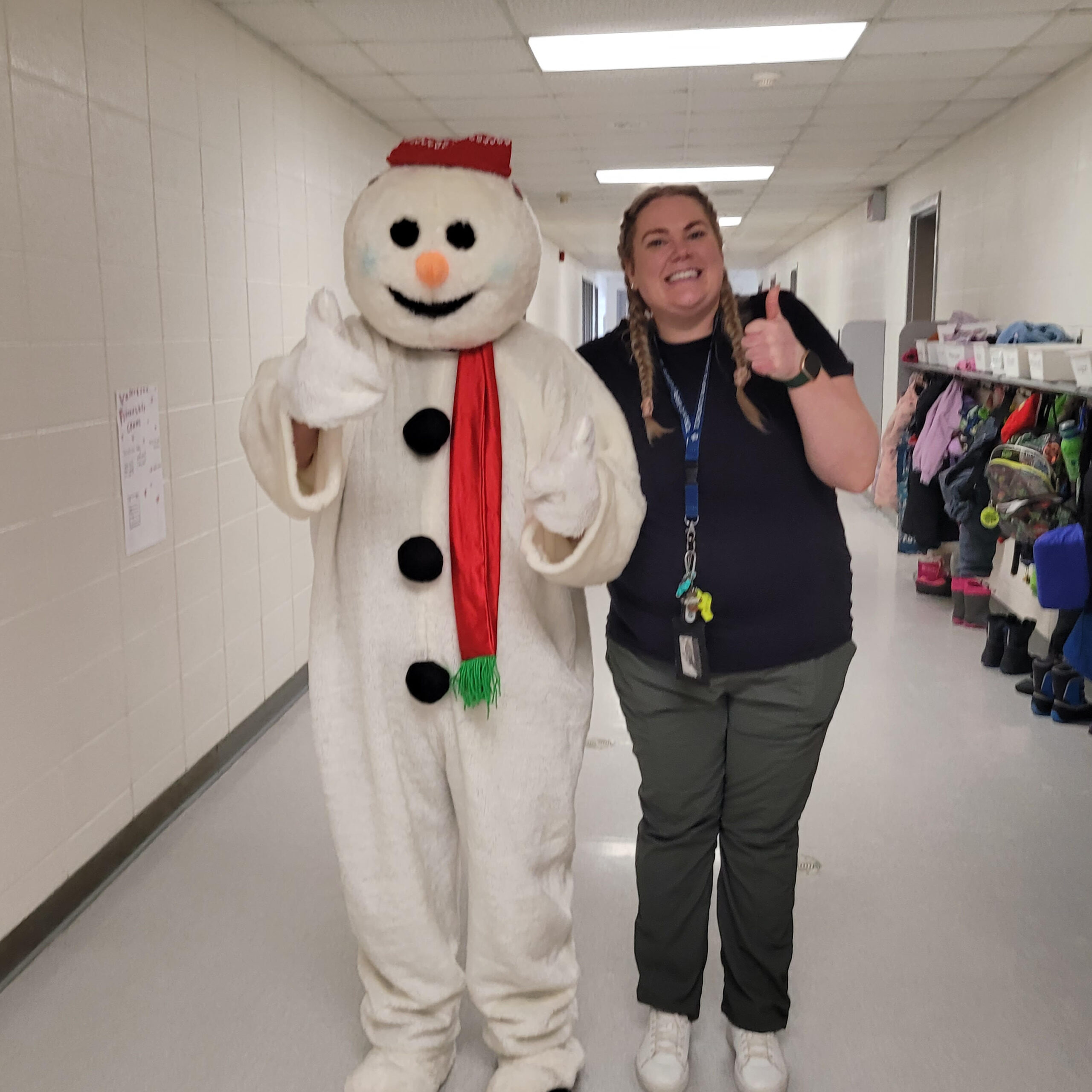 A smiling staff member poses with Bonhomme in the school hallway 